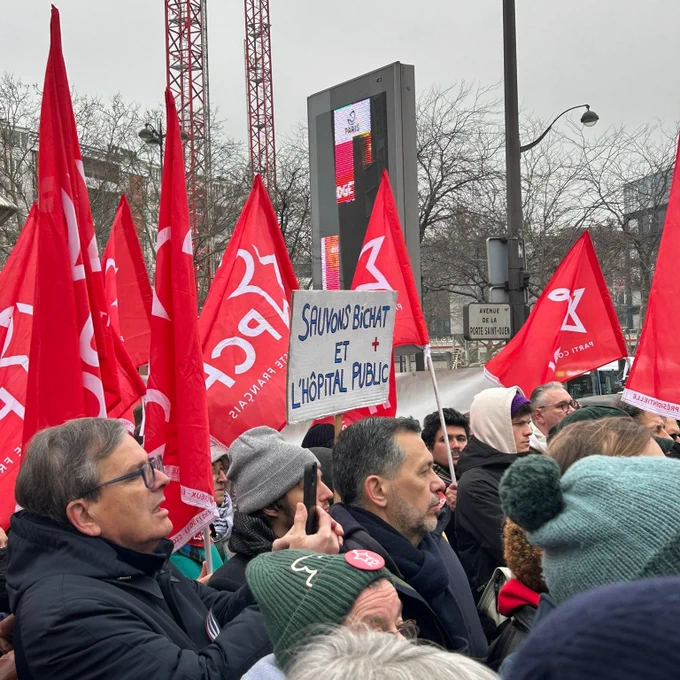 Des personnes debout dans une manifestation avec des drapeaux et une pancarte où est écrit : sauvons Bichat et l'hôpital public 