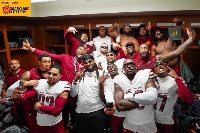 Photo of a group of players posing in the locker room postgame. 