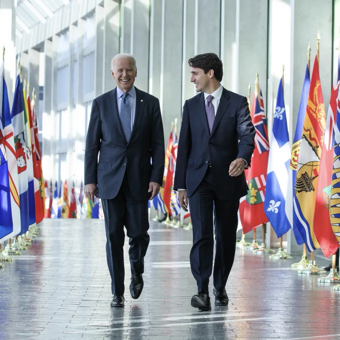 Prime Minister Justin Trudeau and President Joe Biden walk down a hallway, lined with Canada’s provincial flags, together in Ottawa, Ontario. 