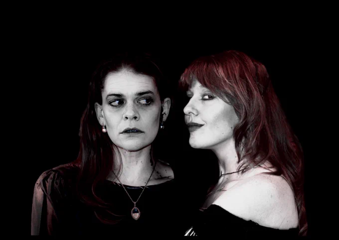 Amy Gavin, on the left, stares out to camera. Hannah, on the right, stares at Amy. Both wearing black with a black background