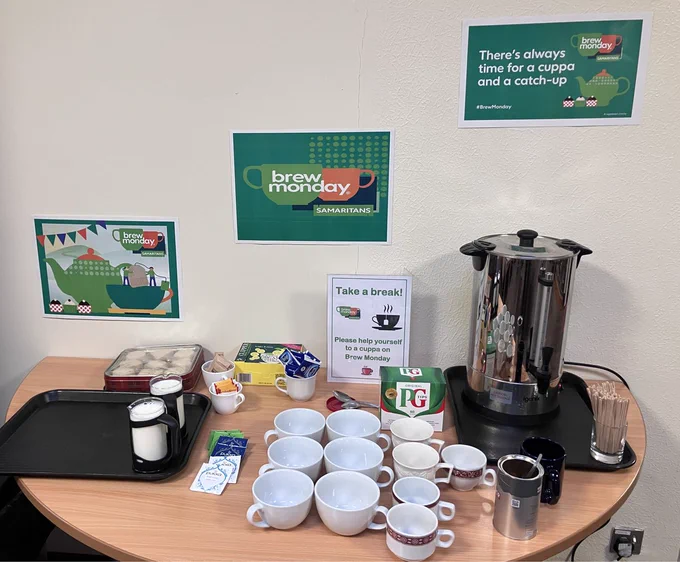 A table containing cups, tea bags, milk, biscuits and brew Monday posters.