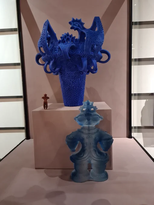 A display of Jomon objects, 'JOMON Vitrified' DUROM.2022.364 A blue glass sculpture. 'Dogu Capsule Toy' a small brown plastic figure. 'Jomon (Blue)' DUROM.2017.332 A large bright blue vase, decorated with lines, handles and markings.
