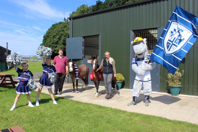 Featherston Rovers Mascot holding a club flag and cheerleaders - all outside the pony discovery centre at the National Coal Mining Museum