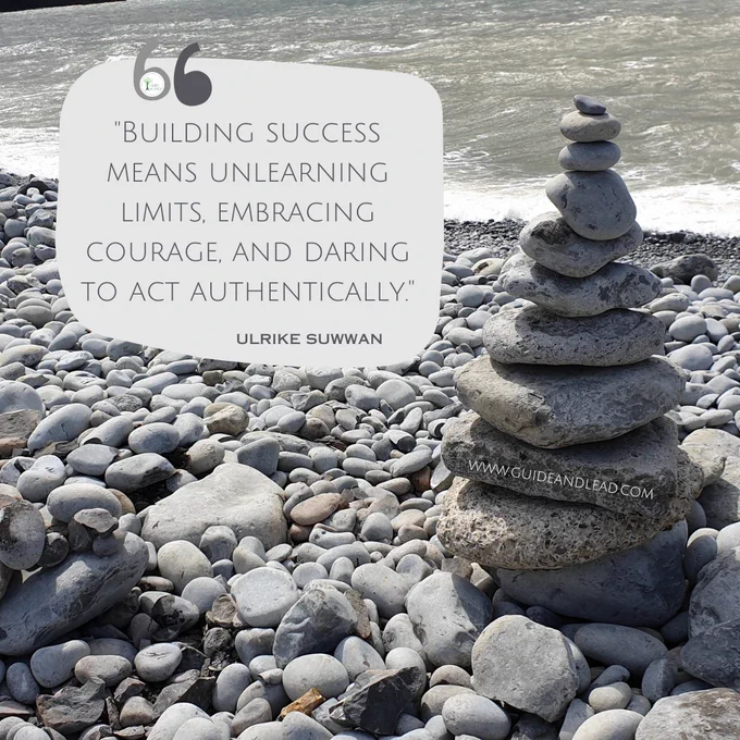 A picture taken at the sea, where stones are placed on top of each other into a tower. Quote"Building success means unlearning limits, embracing courage, and daring to act authentically." Ulrike Suwwan
