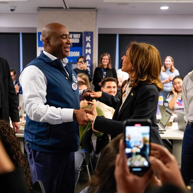 DNC Chair Jaime Harrison holding hands with Vice President Kamala Harris, surrounded by DNC employees and volunteers.