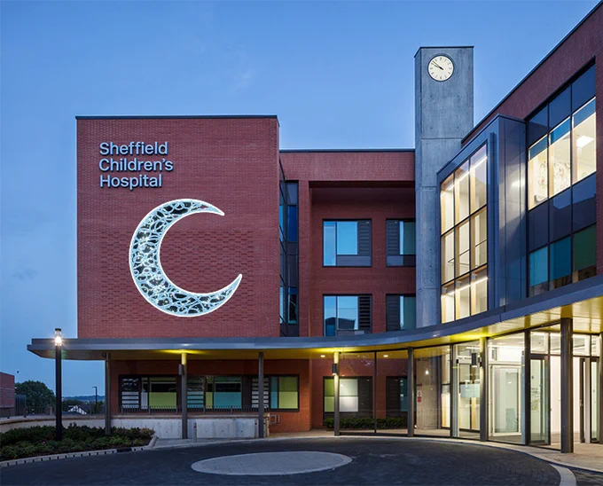 Sheffield Children's Hospital at dusk. A drawing of a crescent moon is imposed onto the side of the hospital.