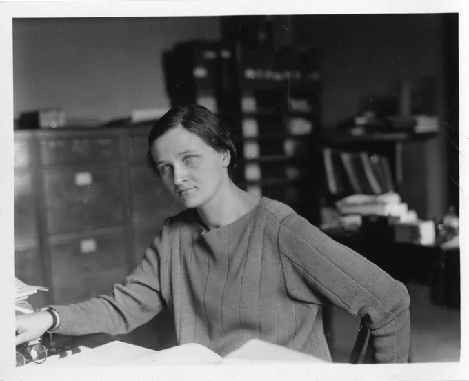 A black and white photo of a woman sitting at a desk.