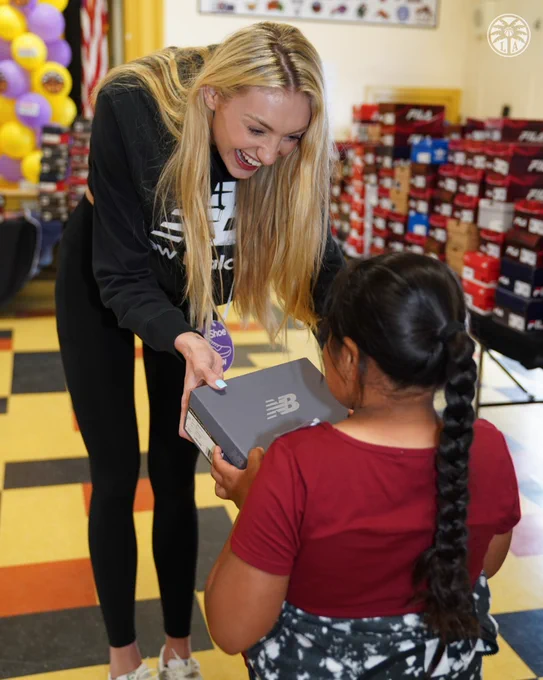 Cameron Brink handing out a pair of New Balance shoes to a kid in need. 