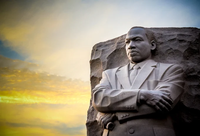 Photo of a statue of Dr. Martin Luther King Jr. with a sunset in the background.