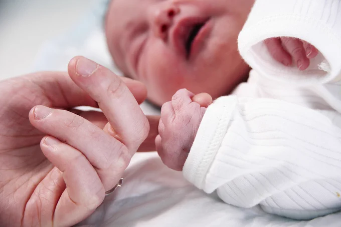 Close up of new born baby holding parents finger