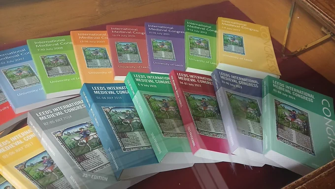 A display of congress programmes in a wooden case dating from mid-2000s to 2024. Covers in blue, green, red and yellow all with the image of St Martin from the Brotherton Library