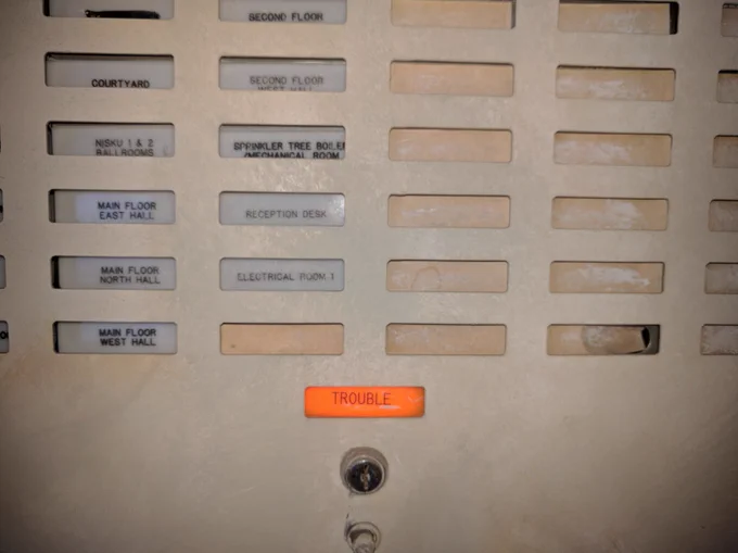 An old, dimly lit fuse box with some different lights corresponding to different parts of the hotel. There's one labelled "TROUBLE" and it's lit up with bright orange.
