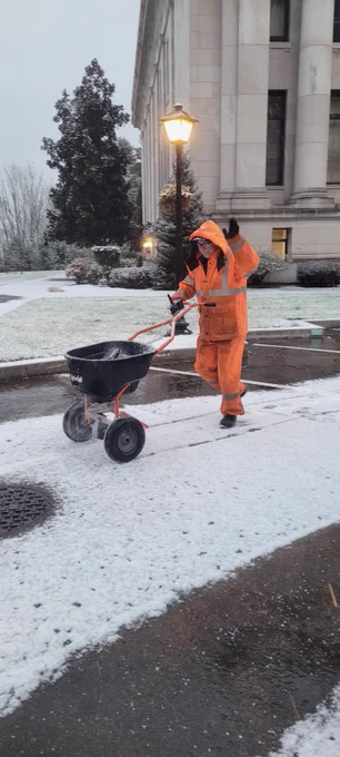 DES staff member wheeling ice melting material onto the campus road. 