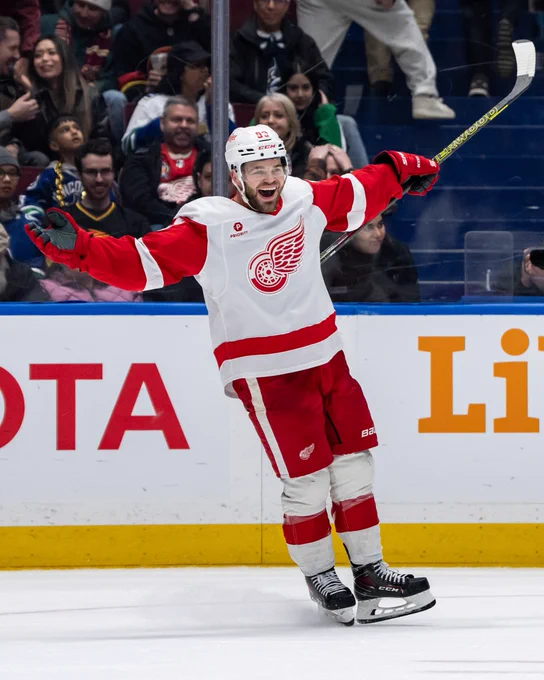 Alex DeBrincat celebrating on ice in a Red Wings uniform.