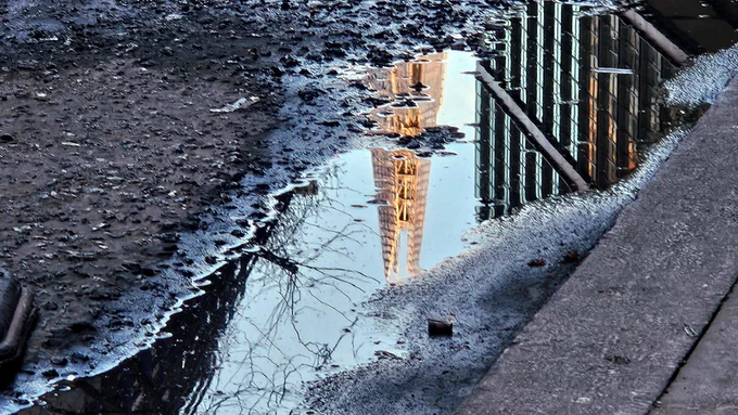 Puddle in a pothole reflecting the Shard building