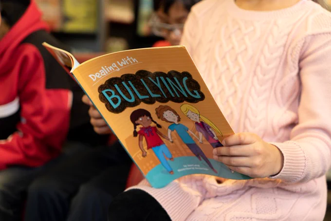 Photo of a child holding a book open. The book title is: 'Dealing with Bullying'.