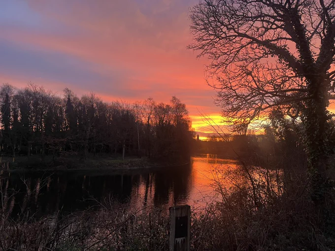 Sunrise reflecting on water in Victoria Park. The water is flowing orange in the morning sun and St Marks church spire is visible in the background.