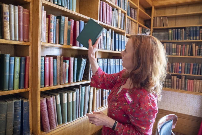 Volunteer putting books back on the shelf in the library at Elizabeth Gaskell's House
