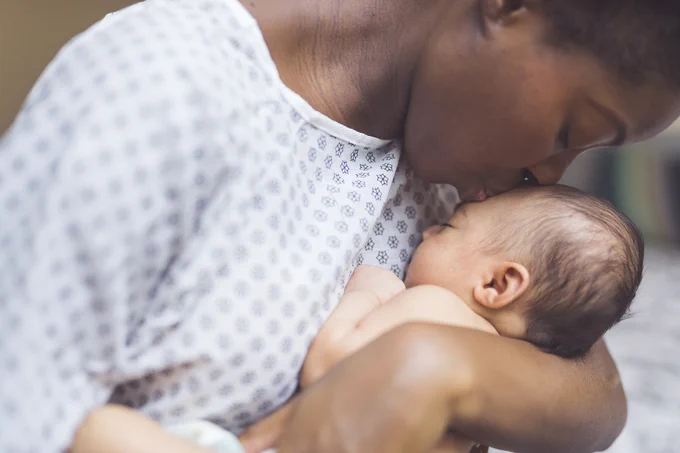 Photo of a woman wearing a hospital gown kissing her newborn on the forehead