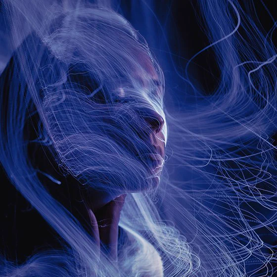Digitally produced abstract image with a black background showing a face emerging through a veil of blue/purple lines and waves enveloping the facial profile
