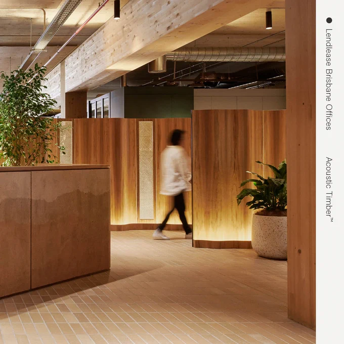 Interior of Landlease Brisbane Offices featuring wooden partition walls and a blurred figure walking past. The design includes exposed wooden beams and potted plants, accentuated by soft lighting.