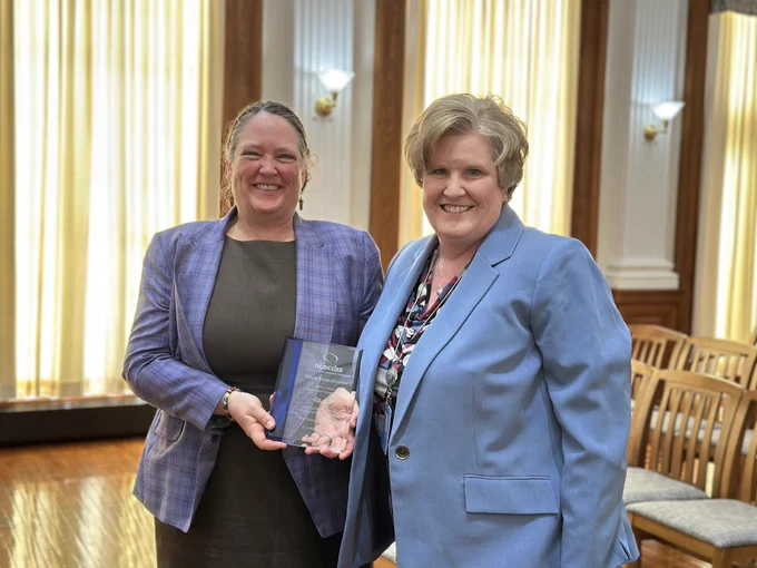 Woman holds glass award standing next to another woman