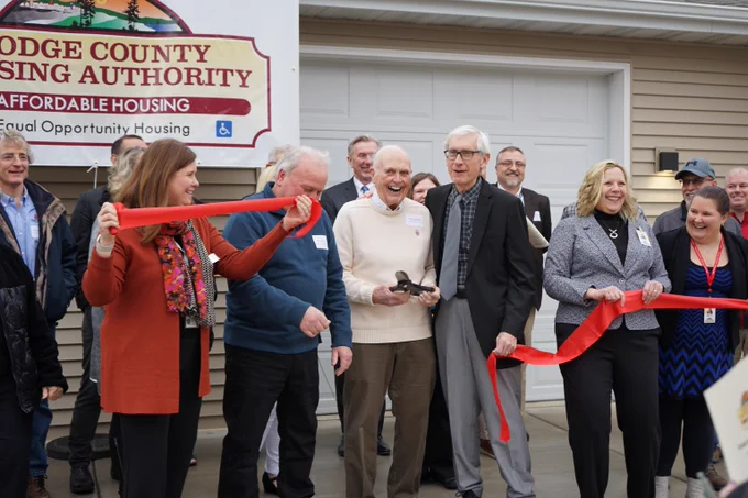 Secretary Kathy Blumenfeld and Governor Tony Evers alongside Donna Braun, Executive Director of Dodge County Housing Authority, Mayor Dan Wegener, City of Juneau, and Glen Stousland, Dodge County Housing Authority Board Chair cutting ribbon in front of Dodge County Housing Authority's affordable housing development in the City of Juneau. 