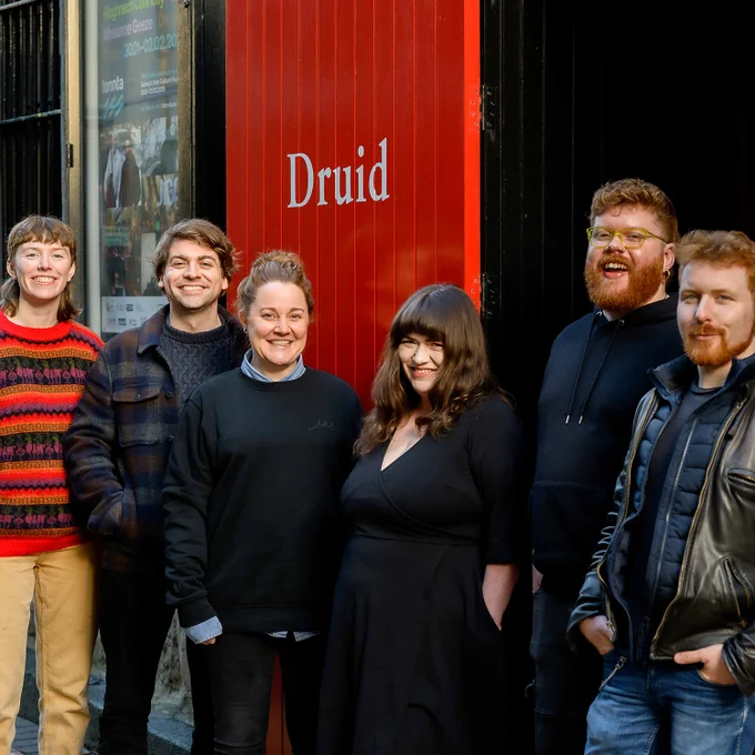 Six people (FUEL 2025 artists and FUEL Programme Manager Síomha Nee) posing together for a group photo outside The Mick Lally Theatre