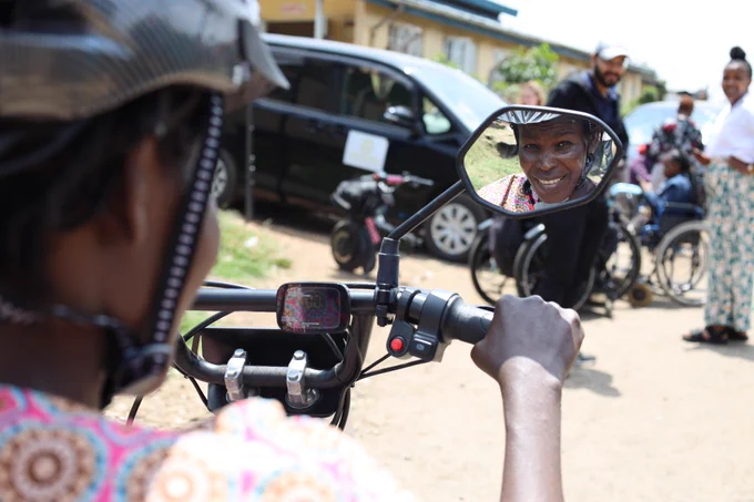 A view from behind a woman on a NeoMotion device, showing her reflection smiling in a rear-view mirror.