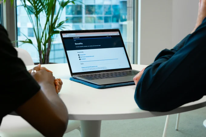 Two people sitting in front of a laptop displaying the topic page for ‘benefits’ on GOV.UK