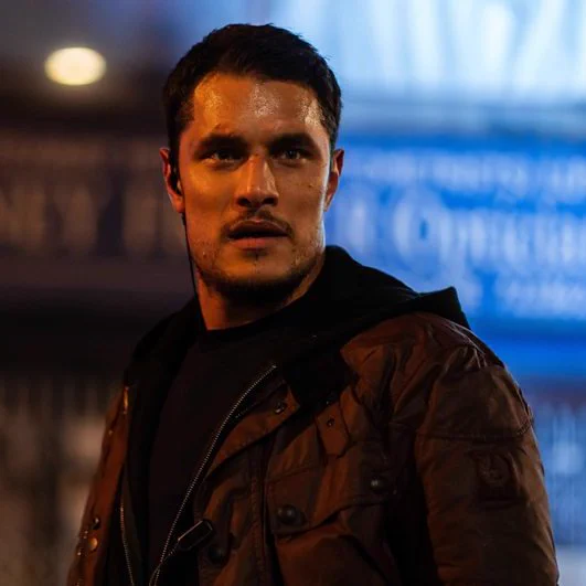 A man stands outside at night looking flustered. He wears a dark jacket over a black top.
