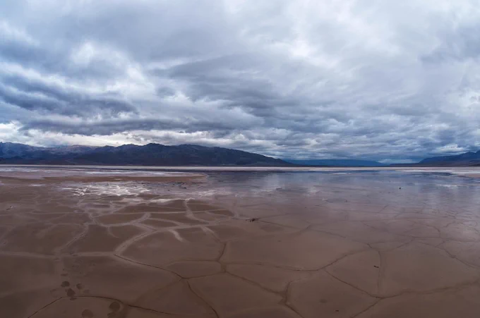 A shallow pool of water over a cracked valley floor underneath a cloudy sky. Photo credit: NPS / Kurt Moses