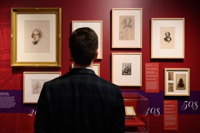 A photo from the new exhibition at the Charles Dickens Museum. A man stands with his back to the camera, facing a wall of illustrations of Charles Dickens.