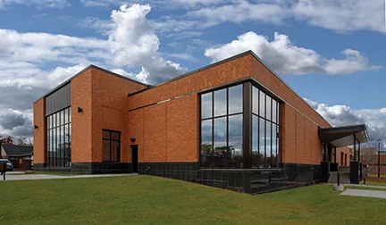 Modern Kaposia Library building with large glass windows and orange brick walls under a blue sky with fluffy clouds.