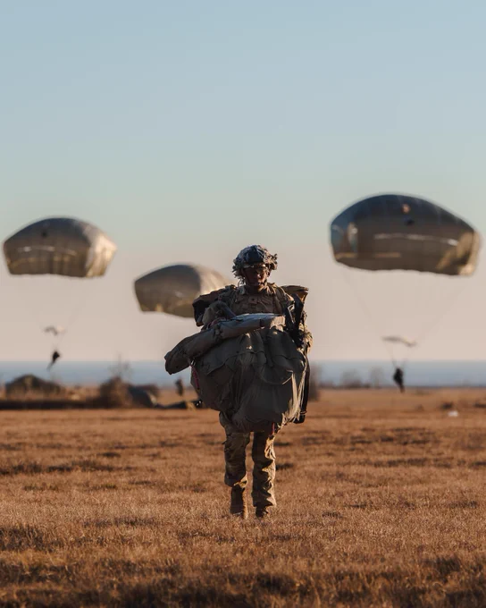 Soldier standing in a field with a parachute on their back.
