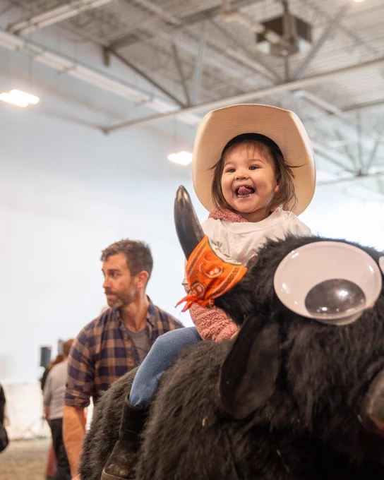 Young child smiling while sitting on a makeshift bull

