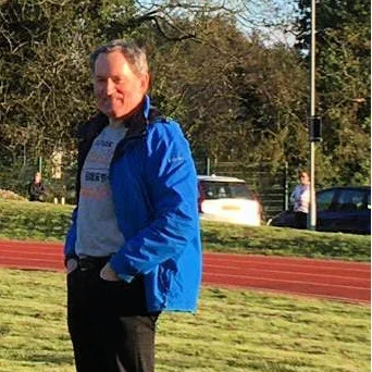 Photo of David Lang on a sunny day looking towards the camera. David is wearing his blue Giffnock North Athletics Club coaching jacket.
