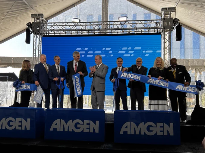 Group of individuals participating in a ribbon-cutting ceremony at an Amgen event, standing behind podiums with the Amgen logo.