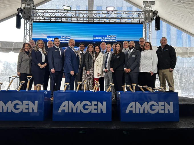 Group of people standing behind podiums with the Amgen logo, at an outdoor event.