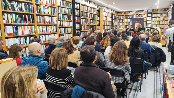 Personas sentadas en una librería escuchando a dos ponentes
