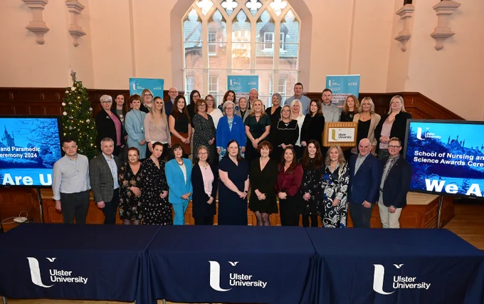 A group of people standing in the hall at the Martha Magee building, flanked either side by TV's that have Ulster University branding for the School of Paramedic Science.