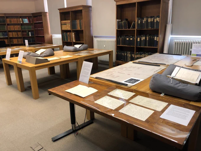 The exhibition space. There are 3 large tables filled with records, letters, plans, books and other objects.