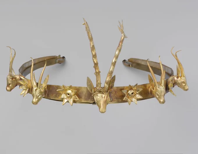 Photo of an Ancient Egyptian gold head ornament made of a band of hammered sheet gold, the ends of which have been tapered to a narrower width and rolled to form loops. The band is decorated with a central head of an antlered stag, flanked on either side by two gazelle heads. Between the animal heads are four 8-pointed flowers or stars. Dimensions: height of central stag 8.9 cm (3 1/2 in); length of headband 49.5 cm (19 1/2 in). Dated c. 1648-1540 BC. Collections The Met, New York.