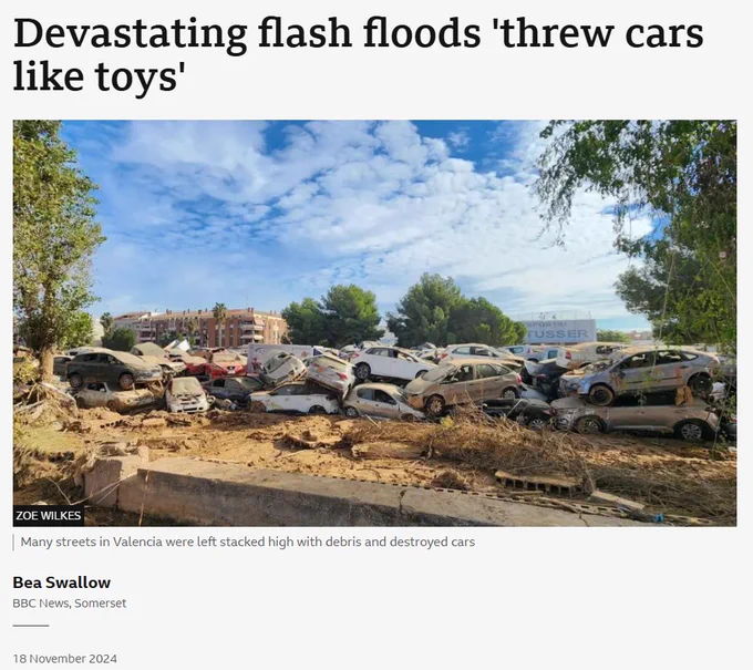 A screenshot taken from a BBC article includes an image of dozens of previously flooded cars, muddy and piled up on a roadside. The headline at the top of the image reads 'Devastating flash flood 'threw cars like toys''