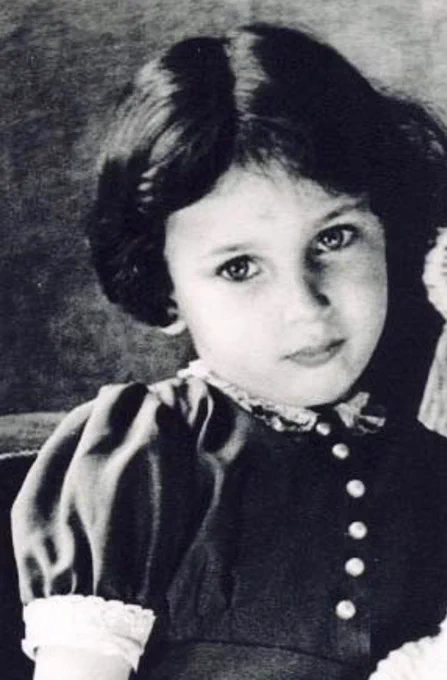 Black and white portrait of a young girl with curly hair, wearing a dark buttoned dress with a collar.
