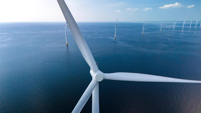 Aerial view of multiple offshore wind turbines in the ocean under a clear sky.