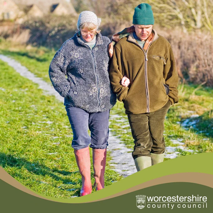A middle-aged couple walking outside wearing fleeces, wellies and winter hats, deep in conversation. At the bottom in a green swish is the white Worcestershire County Council logo. 