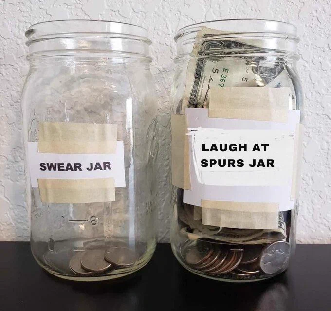 Two glass jars on a shelf labelled with white tape; the left jar labelled "SWEAR JAR" is virtually empty, while the right jar labelled "LAUGH AT SPURS JAR" contains loads of coins and notes.