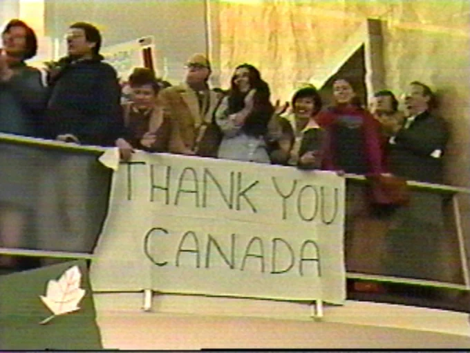 This photo shows a group of people standing behind a barrier, holding up a banner that reads "THANK YOU CANADA." The setting appears to be indoors, possibly at an event or a public gathering. The banner is prominently displayed, and there is a maple leaf symbol on the left side of the image, reinforcing the Canadian theme. The people in the photo seem to be expressing gratitude, likely towards Canada for some form of support or action. The atmosphere looks celebratory or appreciative. 