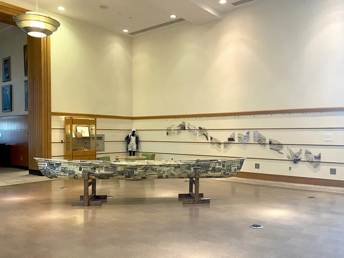 Photo of environmental art installation that includes a canoe, wall art, and other items in the Mann Library Gallery. 